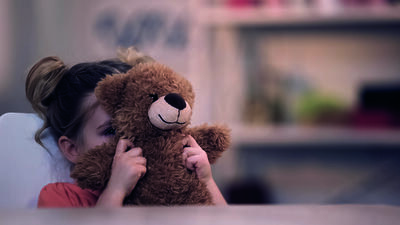Sad female kid covering face by teddy bear toy, family problem, loneliness abuse