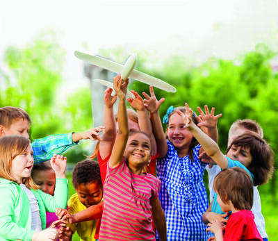 Close-up view of kids reaching after big white airplane toy with arms standing close in the field during summer day