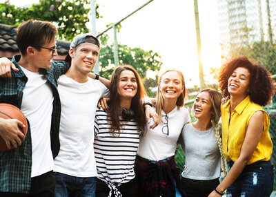 Smiling happy young adult friends arms around shoulder outdoors 
