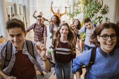 Large group of cheerful students running through school hallway.