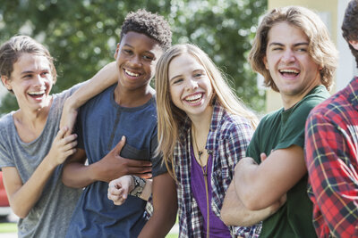 A multi-ethnic group of teenagers hanging out together outdoors. They are in a row, laughing and smiling.